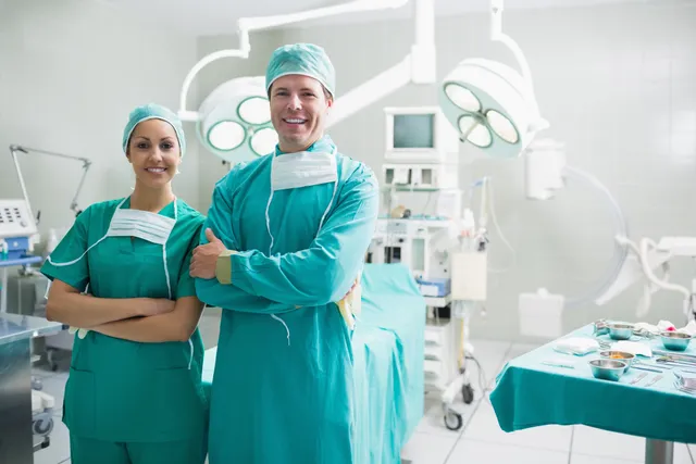 Two doctors in a hospital operating room with their arms crossed.